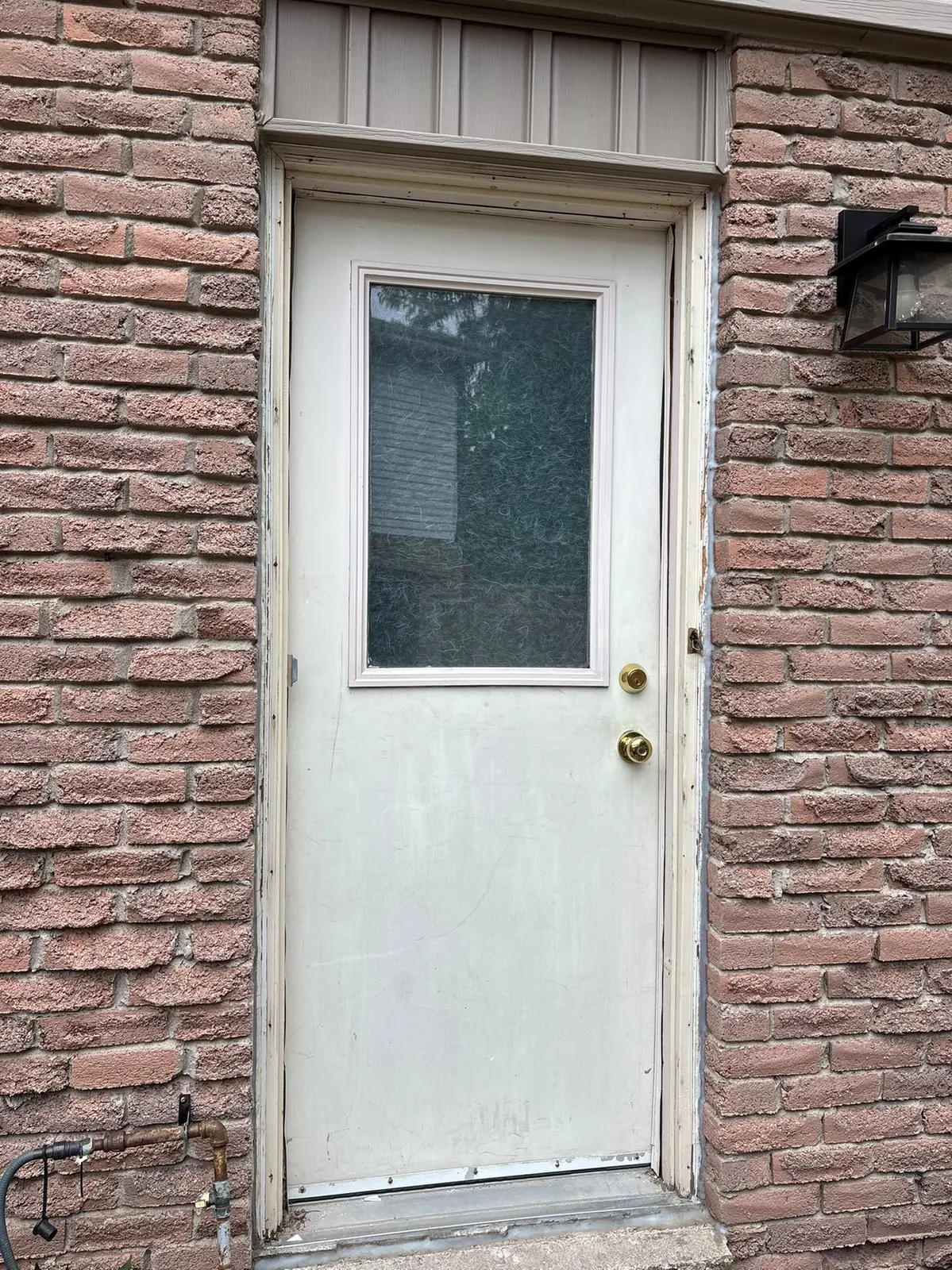 Before: worn white back door with a dark window in a brick wall