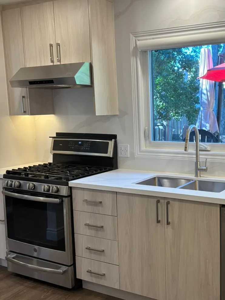After: the same kitchen with wood-grain cabinets, white stone-look counters and backsplash, and new plank flooring