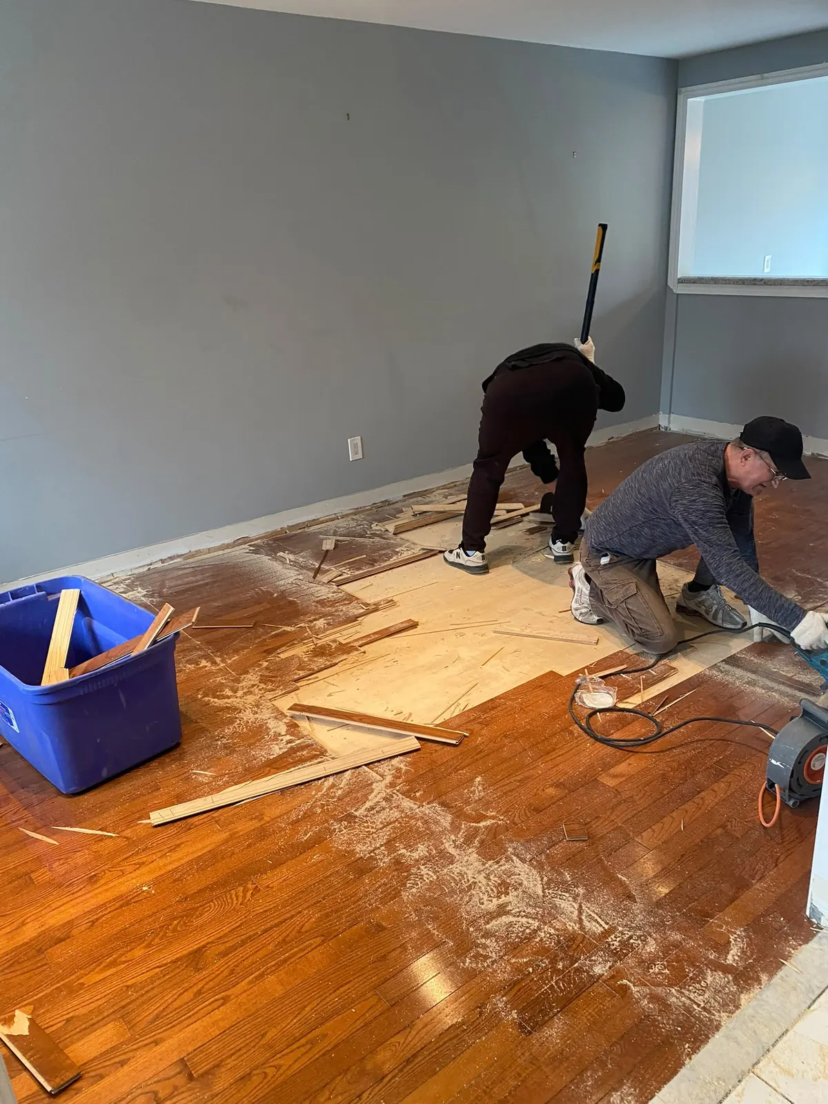Crew removing worn hardwood flooring from a living room