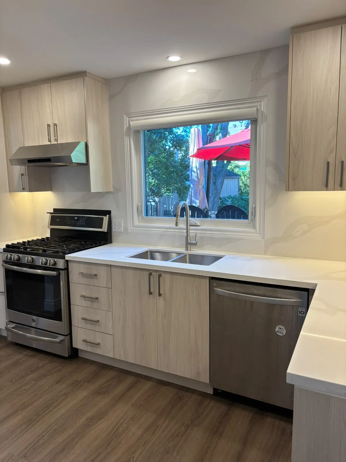 Renovated kitchen with wood-grain cabinets, a white stone-look backsplash, under-cabinet lighting and a window over the sink