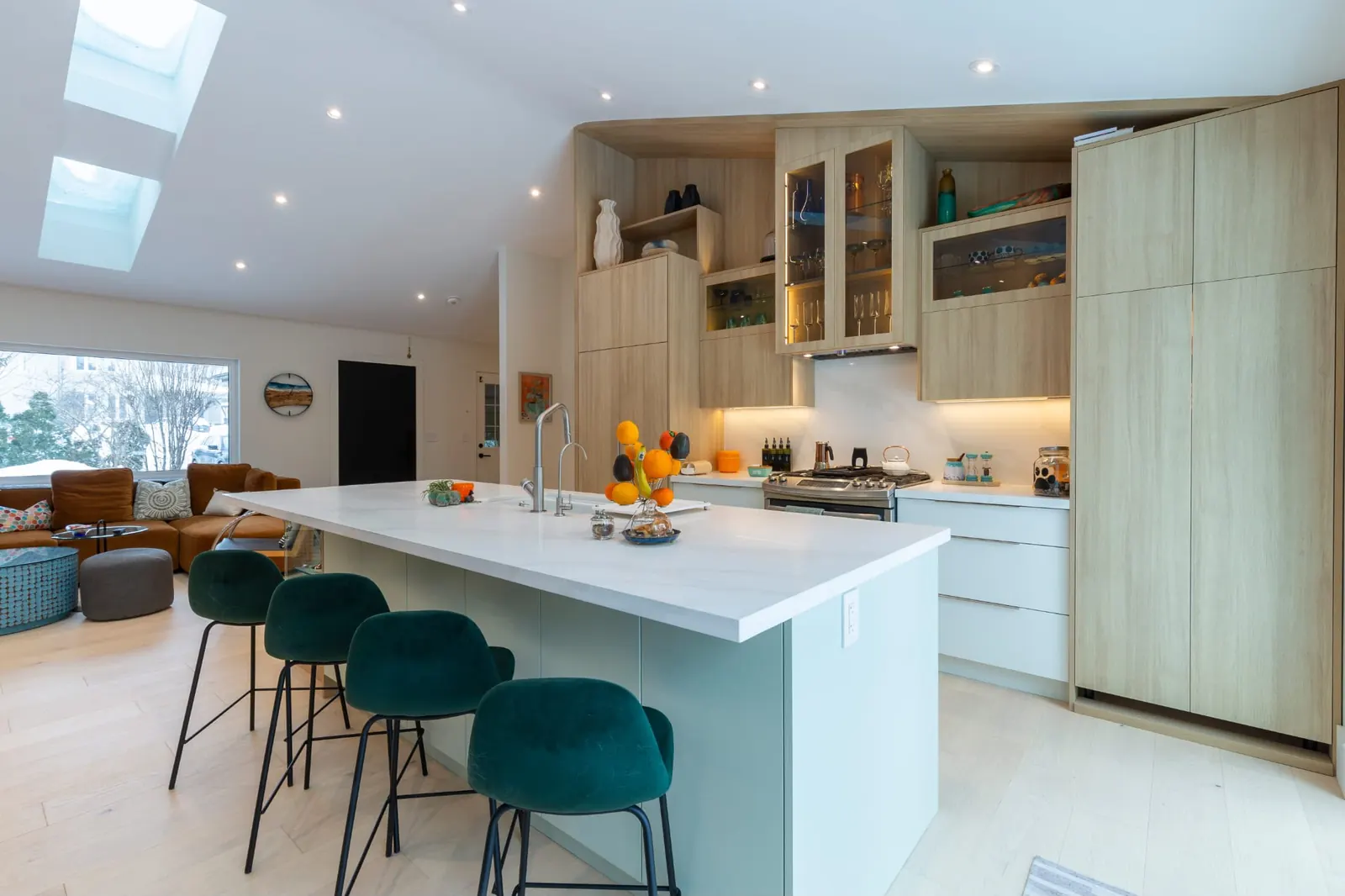 Bright open-concept kitchen and living space with a large island, green bar stools and skylights